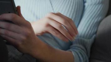 Bol de pop-corn à côté de jeune femme blanche qui prend du pop-corn, assis avec un casque sur les oreilles, regardant la tablette sur les genoux, met du pop-corn dans la bouche, mâche, la lumière de l'écran se reflète sur les yeux video