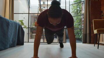 Black man with hands and toes on floor, stretched body, bending one leg, moving it in various directions, changing leg doing same exercise video