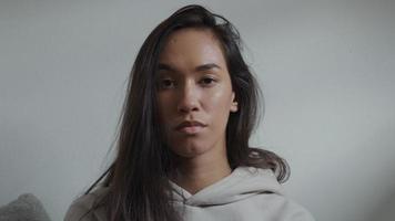 Young mixed race woman with eyes down, lifts head slightly, eyes looking into camera lens, eyes looking down again video