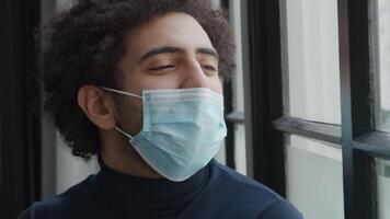 Close up and slow motion of young Middle Eastern man with face mask, looks through window, talks, face mask goes down, hand adjusts face mask on nose video