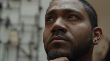 Close up of black man, hand touches chin, eyes looking up to the left, to the right, one eyebrow moves, man looks into camera lens, contemplatively video
