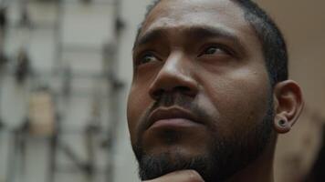 Close up of black man, hand on chin, looking up, to the left, to the right contemplatively, moves eyebrow and looks into camera lens video