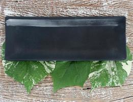 Top view of an empty ceramic plate with leaves on a wood table background photo