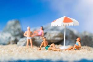 Gente en miniatura vistiendo trajes de baño relajándose en la playa con un fondo azul, concepto de verano foto