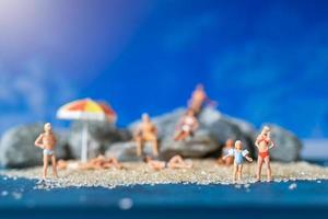 Gente en miniatura vistiendo trajes de baño relajándose en la playa con un fondo azul, concepto de verano foto