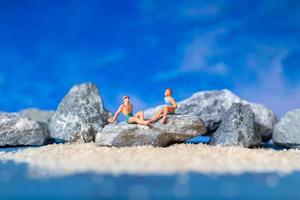 Miniature people wearing swimsuits relaxing on the beach with a blue background, summertime concept photo