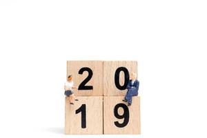 Miniature people sitting on wooden block number 2019 photo