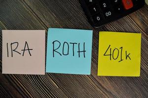 IRA, ROTH, 401k written on sticky note isolated on wooden table