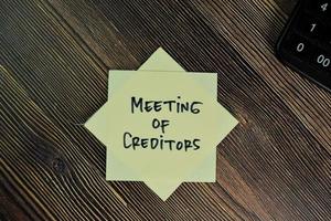 Meeting of Creditors written on sticky note isolated on wooden table photo