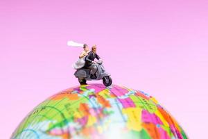 Miniature couple riding a motorcycle on a world globe photo