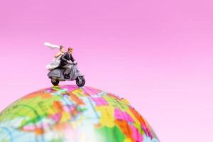 Miniature couple riding a motorcycle on a world globe photo