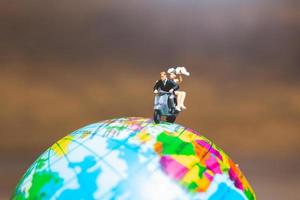 Miniature couple riding a motorcycle on a world globe photo