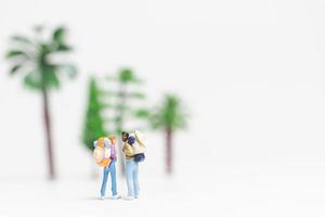 Miniature travelers with backpacks walking on a white background, travel and adventure concept photo