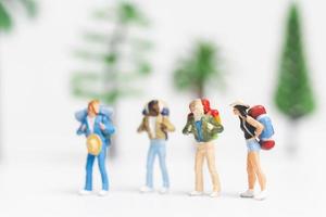 Viajeros en miniatura con mochilas caminando sobre un fondo blanco, concepto de viaje y aventura