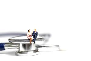 Miniature people sitting on a stethoscope on a white background, health care concept photo