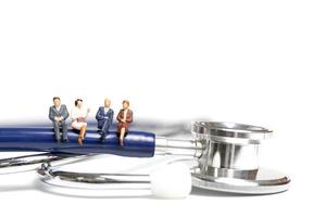 Gente en miniatura sentada sobre un estetoscopio sobre un fondo blanco, el concepto de atención médica foto