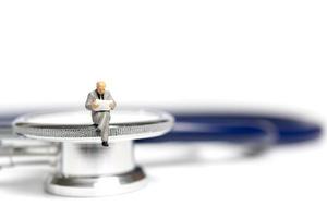 Miniature people sitting on a stethoscope on a white background, health care concept photo