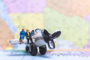 Miniature people sitting on an airplane with a world map background, travel concept photo