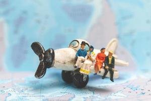 Miniature people sitting on an airplane with a world map background, travel concept photo