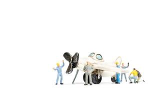 Trabajadores en miniatura que reparan un avión de juguete sobre un fondo blanco. foto