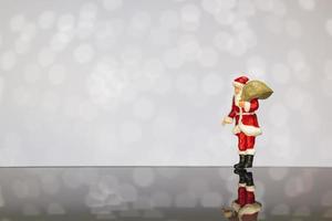 santa claus en miniatura con una bolsa sobre un fondo bokeh, feliz navidad y feliz año nuevo concepto. foto