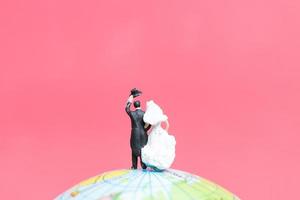 La novia y el novio en miniatura en un globo terráqueo con un fondo de color rosa, concepto de día de San Valentín foto