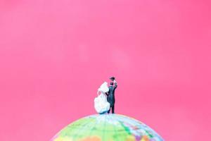 Miniature bride and groom on a globe with a pink background, Valentine's Day concept photo