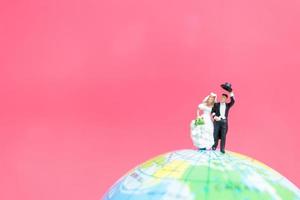 Miniature bride and groom on a globe with a pink background, Valentine's Day concept photo