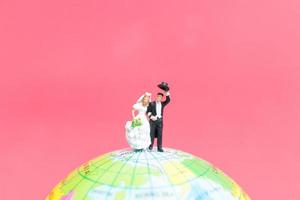 La novia y el novio en miniatura en un globo terráqueo con un fondo de color rosa, concepto de día de San Valentín foto