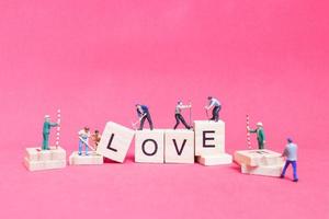 Trabajador en miniatura que se une para construir la palabra amor en bloques de madera con un fondo rosa, concepto del día de San Valentín foto