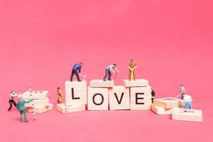 Trabajador en miniatura que se une para construir la palabra amor en bloques de madera con un fondo rosa, concepto del día de San Valentín foto
