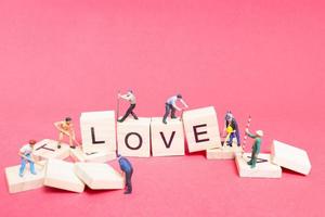 Miniature worker teaming up to build the word Love on wooden blocks with a pink background, Valentine's Day concept photo