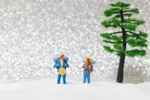 Miniature backpackers walking on a snow background, winter concept