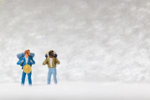 Miniature backpackers walking on a snow background, winter concept