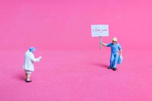 Miniature person holding a paper board with I love you on a pink background, Valentine's Day concept photo