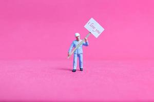 Persona en miniatura sosteniendo un tablero de papel con te amo sobre un fondo rosa, concepto del día de San Valentín foto