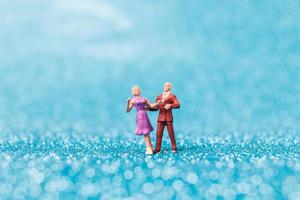 Miniature couple dancing on blue glitter background, Valentine's Day concept photo