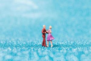 Miniature couple dancing on blue glitter background, Valentine's Day concept photo