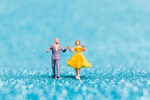 Miniature couple dancing on blue glitter background, Valentine's Day concept photo