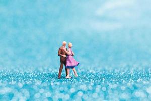 Miniature couple dancing on blue glitter background, Valentine's Day concept photo