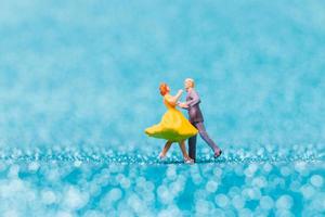 Miniature couple dancing on blue glitter background, Valentine's Day concept photo