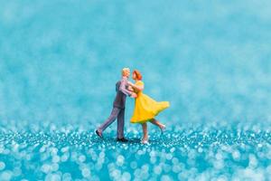 Miniature couple dancing on blue glitter background, Valentine's Day concept photo