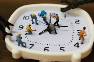 Equipo en miniatura trabajando en un reloj despertador, concepto de tiempo de trabajo foto