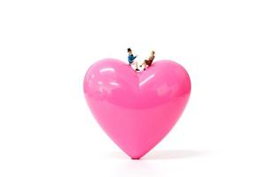 Pareja en miniatura con un corazón de color rosa sobre un fondo blanco, el concepto de San Valentín foto