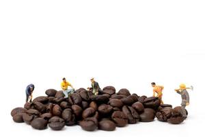 Gente en miniatura que trabaja con granos de café tostados sobre un fondo blanco, concepto de tiempo de café foto