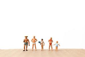 Miniature people wearing swimsuits standing on the beach, vacation concept photo