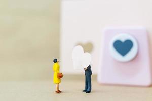 Miniature couple with a paper heart on wooden background, Valentine's Day concept photo