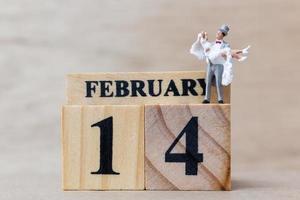 Miniature couple with wooden blocks 14 February text on a wooden background, Happy Valentine's Day concept photo