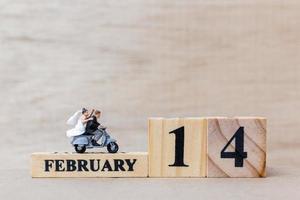 Pareja en miniatura con bloques de madera, texto del 14 de febrero sobre un fondo de madera, feliz día de San Valentín concepto foto