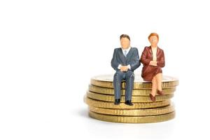 Empresarios en miniatura sentados en una pila de monedas, dinero y concepto financiero foto